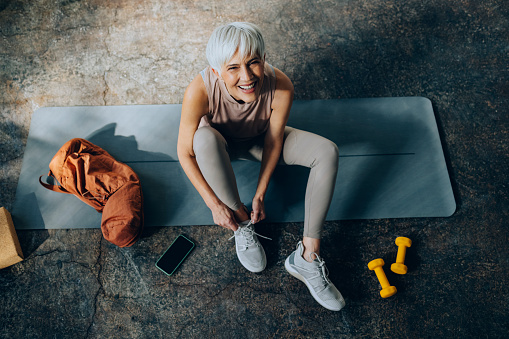 Smiling woman sitting on a exercise mat and  getting ready for fitness training.