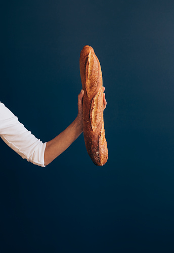 An anonymous female baker holding baked bread in hand while standing over a blue background.