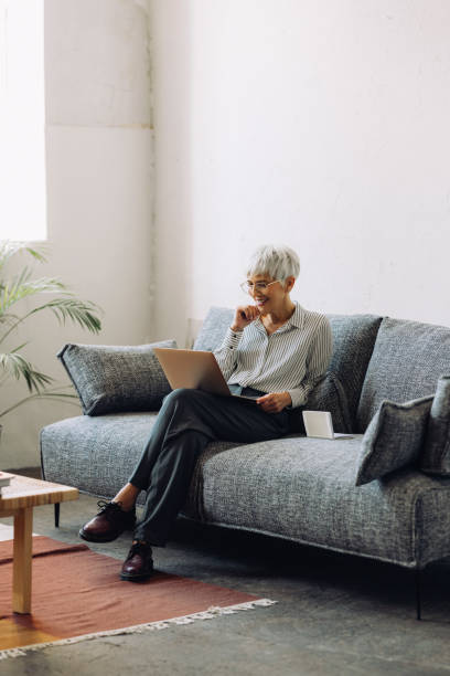 starsza kobieta korzystająca z laptopa w domu - biała kobieta czyta w okularach zdjęcia i obrazy z banku zdjęć