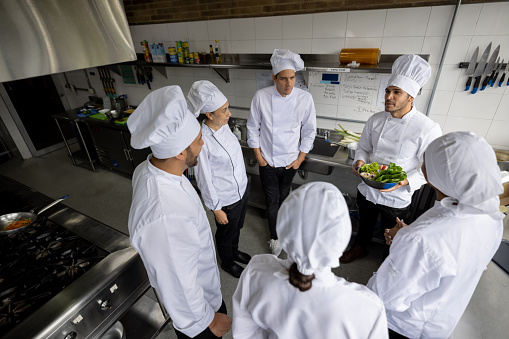 Head chef talking to a group of cooks in the kitchen of a restaurant and explaining the preparation of a plate - food service concepts