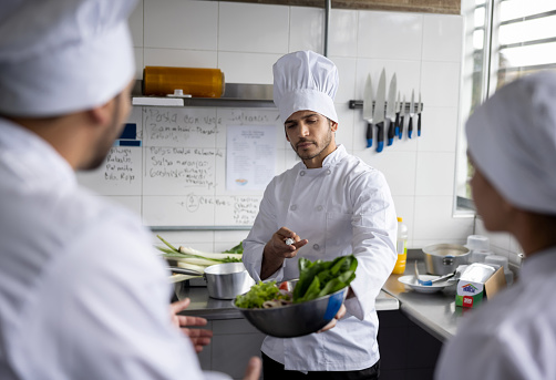 Head chef at a commercial kitchen giving instructions to a group of cooks about the food preparation at a restaurant
