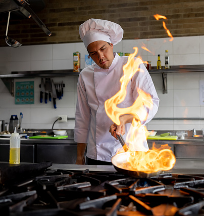 Latin American chef cooking at a restaurant and sauteing vegetables in a pan - preparing food concepts
