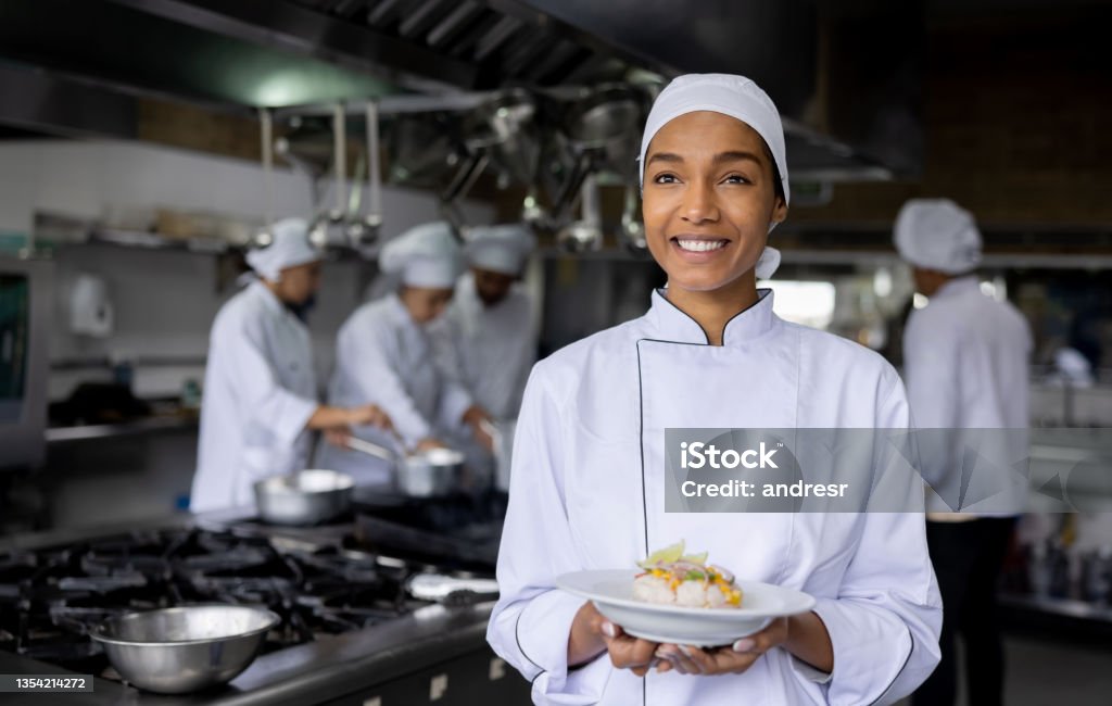 Happy cook preparing food at a restaurant and presenting a plate Happy African American female cook preparing food at a restaurant and presenting a plate while smiling - food service concepts Chef Stock Photo