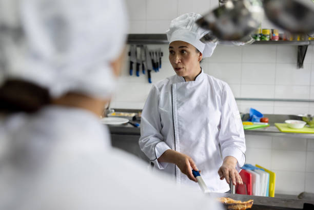 szef kuchni wyjaśnia grupie kucharzy, jak przygotować talerz - teacher preparation two people teamwork zdjęcia i obrazy z banku zdjęć