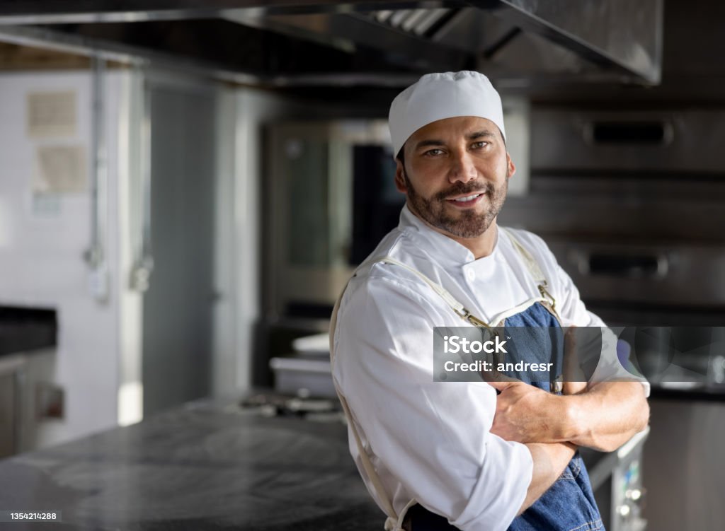 Happy cook working in the kitchen of a restaurant and smiling Portrait of a happy cook working in the kitchen of a restaurant and looking at the camera smiling - food service occupation concepts Baker - Occupation Stock Photo