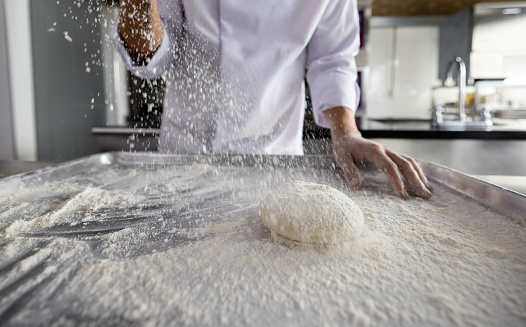 Close-up on a baker sprinkling flour while making bread at the bakery