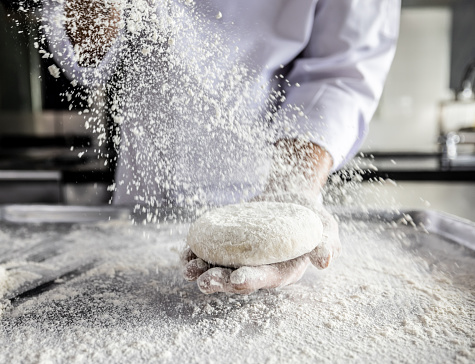 Close-up on a baker kneading the dough at the bakery and sprinkling flour