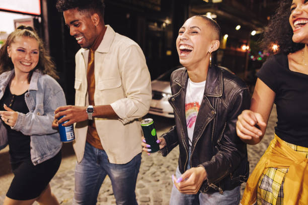 quatro amigos rindo alegremente na cidade à noite - young adult lifestyles city life drinking - fotografias e filmes do acervo