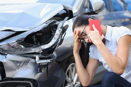 Mujer triste hablando por teléfono celular cerca de auto destrozado photo