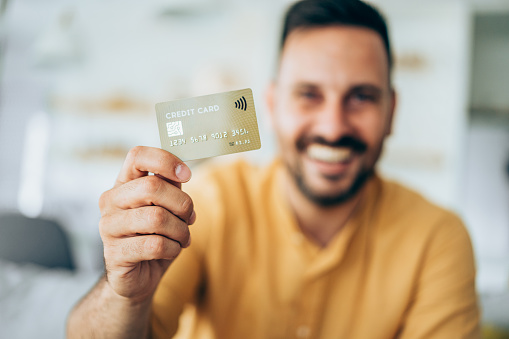 Smiling young businessman holding credit card. Focus is on the card.