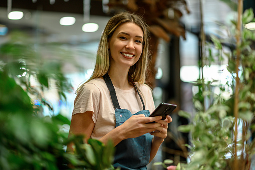 Florist using smartphone while surrounded with flowers and plants in a flower shop