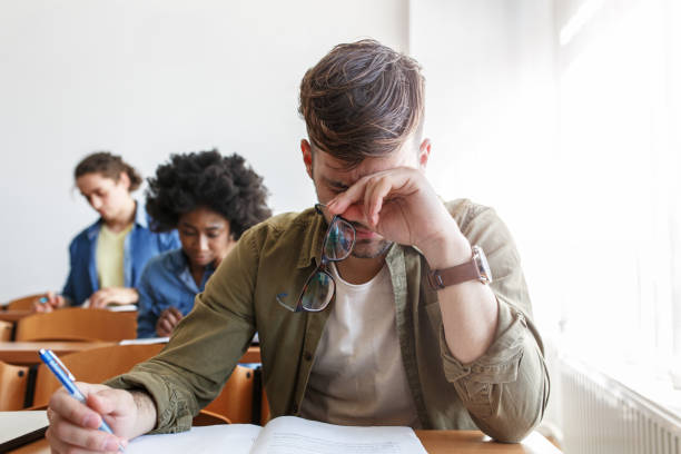 Portrait of young male university student taking a test in a classroom.Trying to resolve problem. stock photo