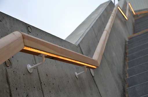 from the bottom of the handle is a recessed LED strip with yellow light. hidden recessed lamp showing a man's palm concrete side of a staircase with retaining walls running through the terrain of a slope, included, uv, covid, disinfection, hygiene, beneath, uderground, below,