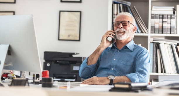 Senior business manager sitting at the desk in his office.He speaks on smart phone. stock photo