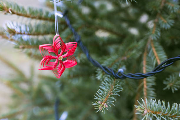 Handmade red paper Christmas star decoration on Christmas tree, outdoors. DIY for children. Environment, recycle, reuse, upcycling, zero waste concept. Selective focus, no snow background