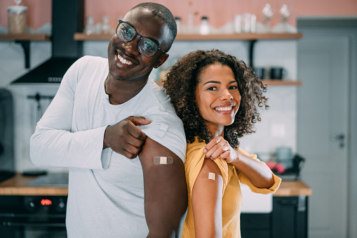 Shot of young afro-american couple showing their arms with a bandage after receiving COVID-19 vaccine. Shot of two young people showing their shoulders after getting coronavirus vaccine.