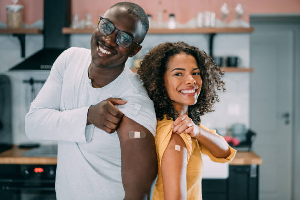 Couple showing their arms after getting vaccinated. Shot of young afro-american couple showing their arms with a bandage after receiving COVID-19 vaccine. Shot of two young people showing their shoulders after getting coronavirus vaccine. adhesive bandage stock pictures, royalty-free photos & images