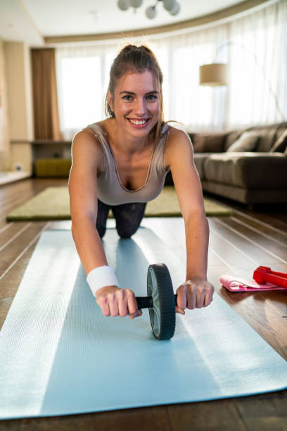 自宅で腹部トレーニングをしている若い女性 - 腹筋ローラー ストックフォトと画像