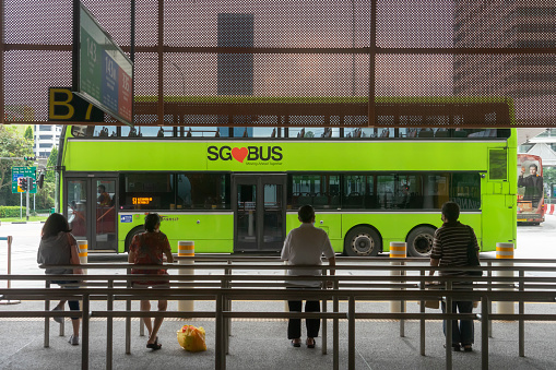 Singapore, Singapore - November 6, 2021: Commuters waiting in line for a bus to arrive at Jurong East Bus Interchange, as one drives off in the background.