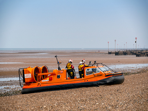 H-003, the ‘Hunstanton Flyer’, an RNLI (Royal National Lifeboat Institution) rescue hovercraft on the South Beach at Heacham in Norfolk, Eastern England. The ‘Hunstanton Flyer’, based in the town of the same name just along the coast, is one of only a few of these H-Class rescue craft, which are used in areas where sands are vast and incoming tides can have fatal consequences when unwary beach-lovers find themselves cut off on a sandbank. Being manoeuvrable in places with shallow water and on sandbanks, the ‘Flyer’ is perfect for this area of The Wash and parts of the North coast of Norfolk. Here, the crew are indicating that onlookers should stand well back as they are about to depart, causing a great deal of spray.