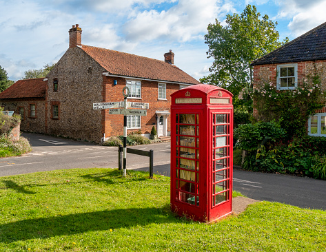 In the pretty village of Great Snoring in Norfolk, Eastern England, the now-defunct red telephone box on the village green has been converted for use as a village library. The box is a K6 type, designed by Sir Giles Gilbert Scott in 1935 and was given listed building status in 1989.\nNear the library is a traditional direction sign with its arms pointing towards Walsingham, Wells. Thursford, Holt, Little Snoring, Norwich and Fakenham.