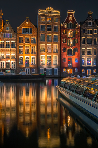 Netherlands. Night Amsterdam. Multi Colored windows of authentic houses near the water and a pleasure boat