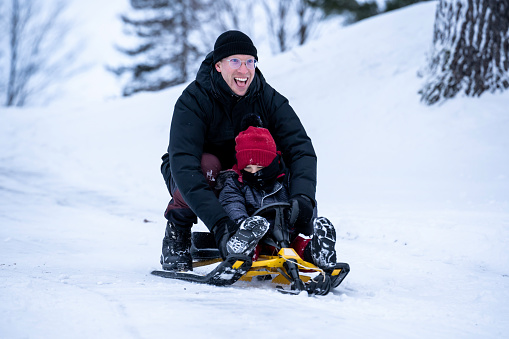 A young boy tobogganing with his uncle during winter in Quebec.