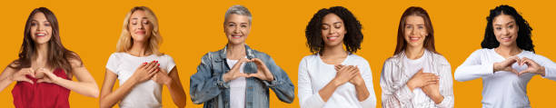 Smiling adult and young european and afro american women press hands to chest, make heart gesture Smiling adult and young european and afro american women press hands to chest, make heart gesture, are grateful and show care sign, isolated on orange background. Positive human emotions, collage heart hands multicultural women stock pictures, royalty-free photos & images