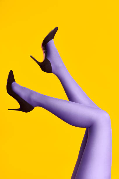 Raised females legs in bright tights and stylish high heels shoes on yellow background stock photo