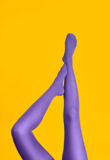 Slim female legs in purple tights raised up on yellow background stock photo