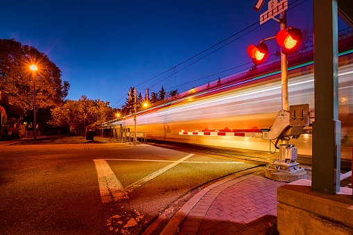 Train passing through road crossing at night with flashing signals and light trails