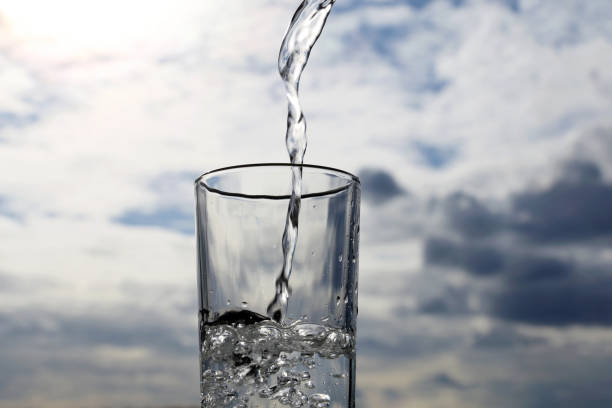 Clean water pouring into drinking glass on background of sky with clouds stock photo