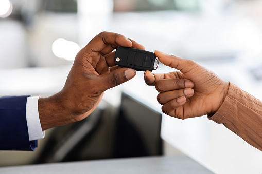 Closeup Shot Of Car Seller Giving Keys To Black Female Customer In Showroom, Unrecognizable African American Woman Buying New Automobile In Dealership Center, Cropped Image, Selective Focus