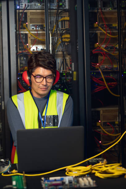 istock Asian male engineer wearing ear plugs using a laptop in computer server room 1354242089