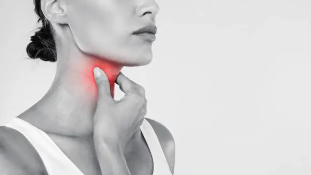 Closeup of sick woman having sore throat, touching her neck with red inflamed zone, suffering from laryngeal disorder, tonsillitis, throat cancer, cold, free copy space over gray studio background
