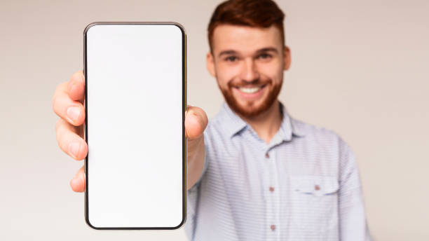 istock Cheerful young businessman showing cellphone with blank screen 1354242703