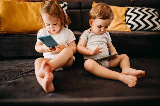 Modern brother and sister use a mobile phone. They watch cartoons and play games