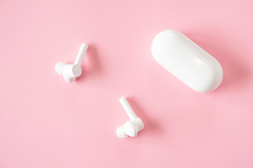 New white earbuds on a bright pink base with lost of copy space.