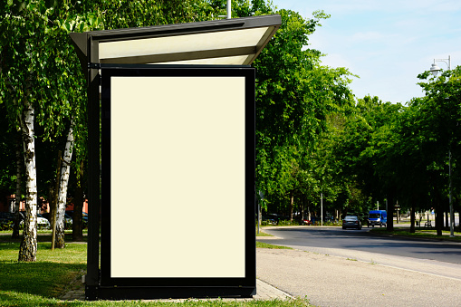 blank white ad panel. bus shelter and bus stop. glass and aluminum frame structure. glass design. composite image. green background. poster sign and commercial banner display. copy space