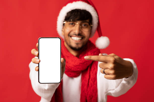 istock Happy indian guy in santa hat showing smartphone, mockup 1354245137
