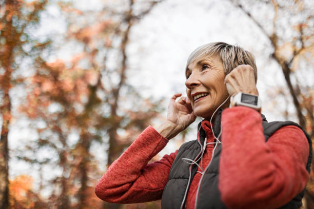 похоженная женщина надевает наушники - senior adult outdoors wellbeing sky стоковые фото и изображения