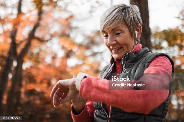 Senior Woman Looking At Smart Watch Wearing Headphones Stock Photo - Download Image Now