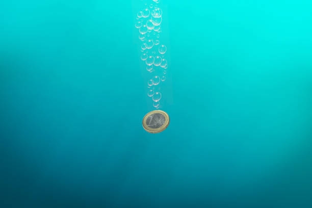 One euro coin sinks in blue water, symbol of lost money