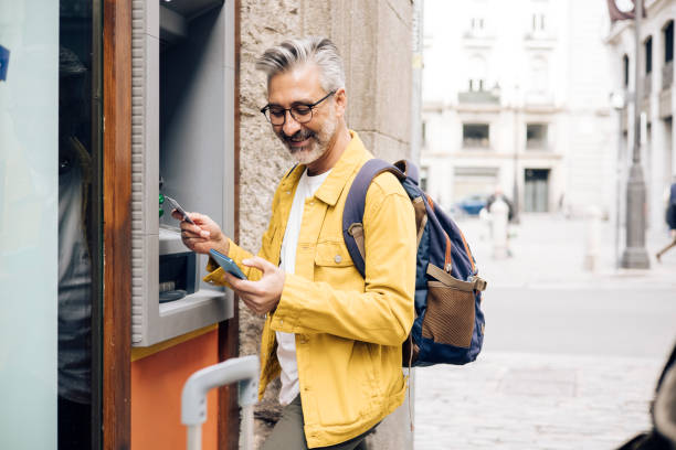 Mature tourist taking the money on the ATM Portrait of a mature tourist in Madrid using ATM. atm stock pictures, royalty-free photos & images