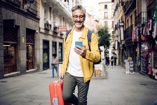 Portrait of a mature man on vacation sightseeing Madrid and using smartphone on the move.