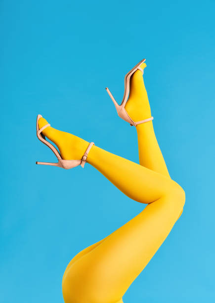 Beautiful legs woman raised up in bright yellow tights and high heels shoes on blue background stock photo