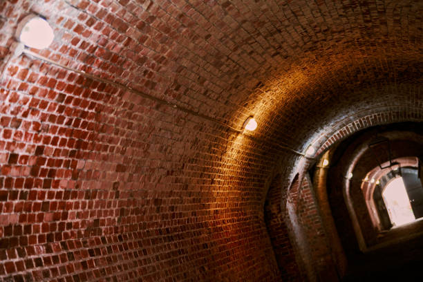 Loft brick tunnel in old German fort, secret passageway with old electricity wiring, Kaliningrad Brick tunnel in old German fort, red brick loft corridor with old wiring, industrial basement of secret military base. Secret passageway of old mansion. Fort No. 5 King Frederick William III kaliningrad stock pictures, royalty-free photos & images