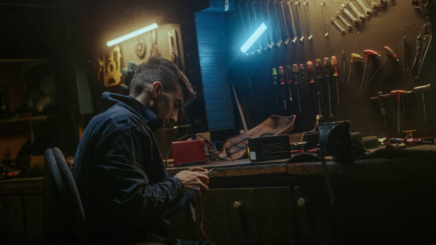 istock Young blacksmith man with workwear standing up and get proper tool for strip the cable, sitting down and working on workbench in his workshop 1354257659