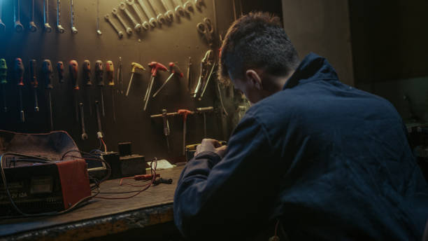 istock Young workshop owner man with workwear, sitting on chair and solder on workbench 1354258938