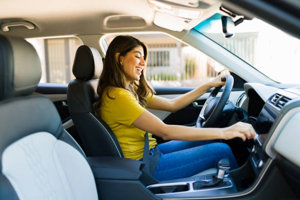 Woman turning up the volume on the car radio Cheerful young woman singing in the car while driving and listening to music on the radio driver stock pictures, royalty-free photos & images